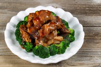 Close up view of barbecued beef ribs, in extra sauce, and broccoli in white plate on rustic wood setting. 
