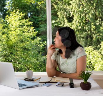Mature woman, looking out window while holding apple in hand, working at home 