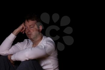 Side view of depressed mature man with eyes closed in thought.  Dark background with copy space available. 

