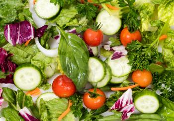 Overhead view of a fresh salad consisting of cherry tomatoes, parsley, basil, onion, cucumber, and green beans. Filled frame format. 