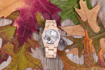 Overhead view of stainless steel watch with autumn leaves and rustic wood. 