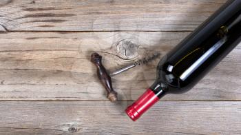Flat view of a bottle of red wine with antique corkscrew opener on rustic wooden boards
