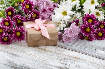 Gift box with colorful mixed flowers in background on white weathered wooden boards 