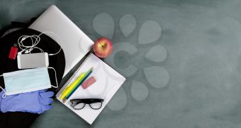 Back to school concept with protective mask and gloves for coronavirus on erased green chalkboard background