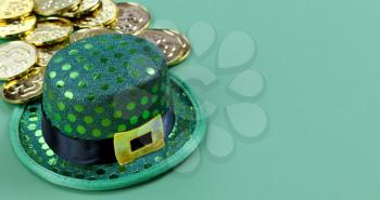 Close up of a St Patricks day Irish elf hat and shiny gold coins in background on green setting with copy space