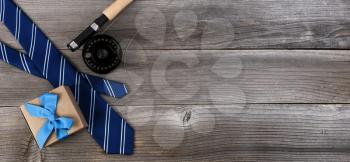 Fathers day concept with blue dress tie, fly fishing reel and a gift box on rustic wooden background in flat lay format