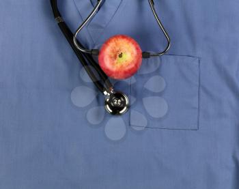 Good health concept with apple fruit and stethoscope placed on blue medical outfit in close up view   