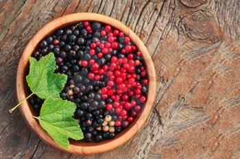 Sweet, black and red currant and green leaves in wooden bowl. Closeup. Selective focus.