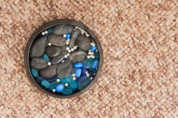 Pearls and colored stones in clay vase on carpet background. Closeup.