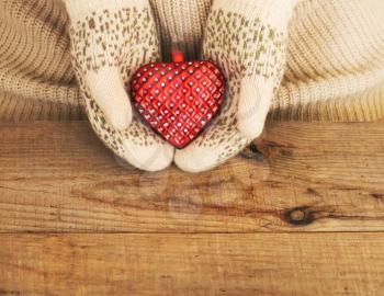 Woman hands in light teal knitted mittens are holding red heart on wooden background. Winter, Valentines day and Christmas concept.