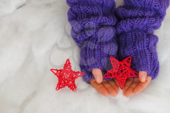 Woman hands in light teal knitted mittens are holding red stars on snow  background. Winter and Christmas concept.