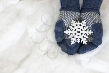 Woman hands in light teal knitted mittens are holding snowflake on snow background. Winter and Christmas concept.