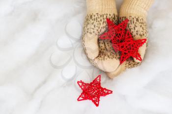 Woman hands in light teal knitted mittens are holding red stars on snow background. Winter and Christmas concept.
