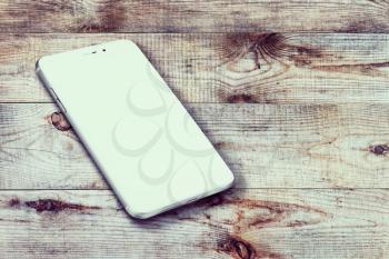 Realistic mobile phone with blank screen and shadows on wooden background. Highly detailed illustration.