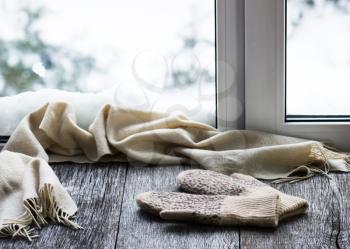 Beige woolen scarf and mittens located on stylized wooden window sill. Winter concept of comfort and relaxation.