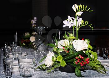 Flower composition of freesia, roses and hypericum on tables set for dining 
