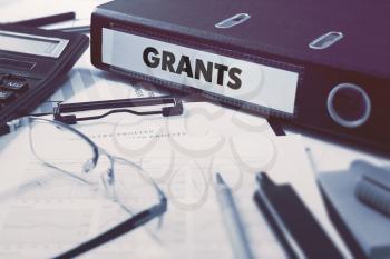 Grants - Office Folder on Background of Working Table with Stationery, Glasses, Reports. Business Concept on Blurred Background. Toned Image.