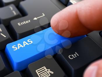 SAAS - Software as a Service - Blue Button - Finger Pushing Button of Black Computer Keyboard. Blurred Background. Closeup View.