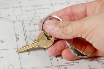 Hand holding a key over house blueprints