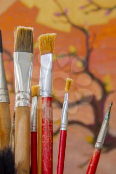Some artistic paintbrushes in front of an unfinished painting.