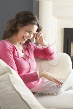 Woman Using Laptop Relaxing Sitting On Sofa At Home Talking On Phone