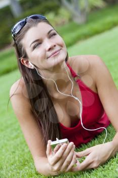A beautiful young brunette woman lying down outside listening to music on her MP3 player