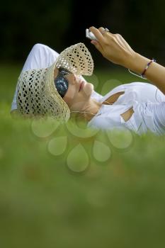 A beautiful dark haired woman laying in a sunlit wooded glade listening to her mp3 player