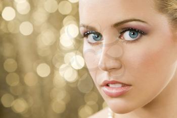 Studio shot of a beautiful young blond model with blue eyes shot against a sparkling gold background.