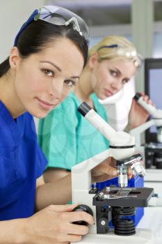 A female medical or scientific researcher or doctor using her microscope in a laboratory with her  colleague out of focus behind her.