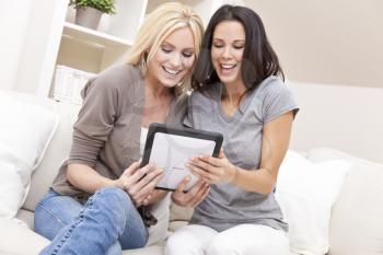 Overhead photograph of two beautiful young women at home sitting on sofa or settee using a tablet PC computer and laughing