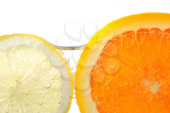 Orange and lemon slices in water with air bubbles on white background