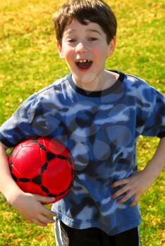 Portrait of a young cute happy boy holding a red soccer ball outside
