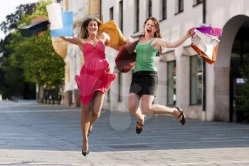 Two women being friends shopping downtown with colorful shopping bags, they are jumping for joy�