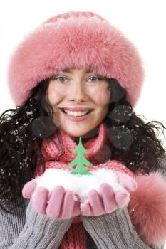 Cheerful woman in pink winter fur cap looking at camera with toy firtree on her palms