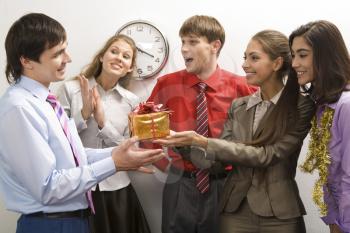 Portrait of friendly colleagues giving birthday present to happy man in office