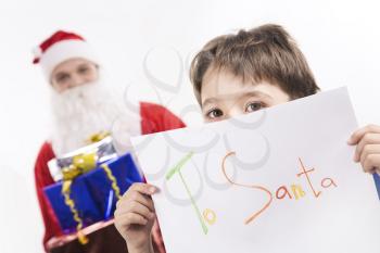 Photo of curious brown-eyed boy peeking out of his letter to Santa Clause