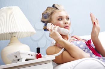 Portrait of female in curlers drying her fingernails and speaking on the telephone