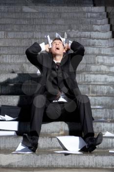 Despaired businessman screaming with papers in hands while sitting on staircase