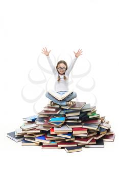 Portrait of cute girl sitting on pile of books with raised arms