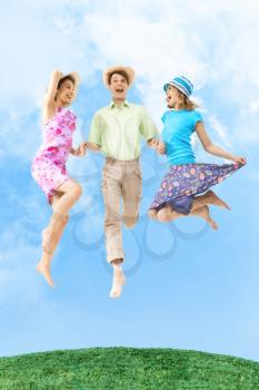 Portrait of joyful girls in jump holding happy man by hands with blue sky on background