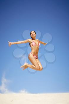 Portrait of joyful girl leaping on sandy beach during summer vacation and laughing