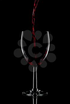 Low key shot of red wine being poured into a glass against a black background.