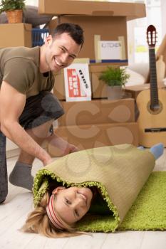 Young couple having fun at moving house, laughing man rolling girlfriend into carpet.