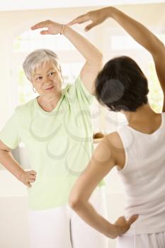 Healthy senior woman doing exercises with personal trainer at home, smiling.