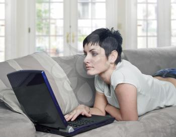 Young women lies on the sofa at home and works on laptop computer.