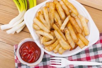 French fries with ketchup and onions on a wooden table.