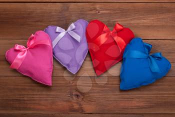 Hearts with ribbons of different colors on a wooden background.