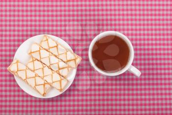 Black tea in a cup and biscuits on the tablecloth.