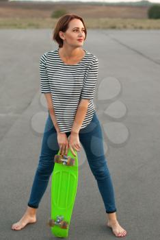 Girl with skateboard standing barefoot on the asphalt.
