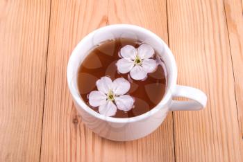 A cup of tea with flowers on a wooden background.